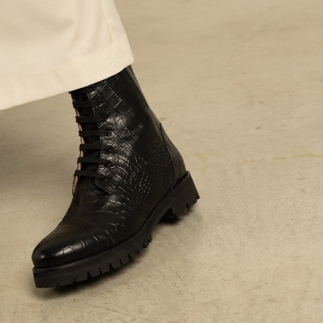 Black leather boot with crocodile texture on a beige background