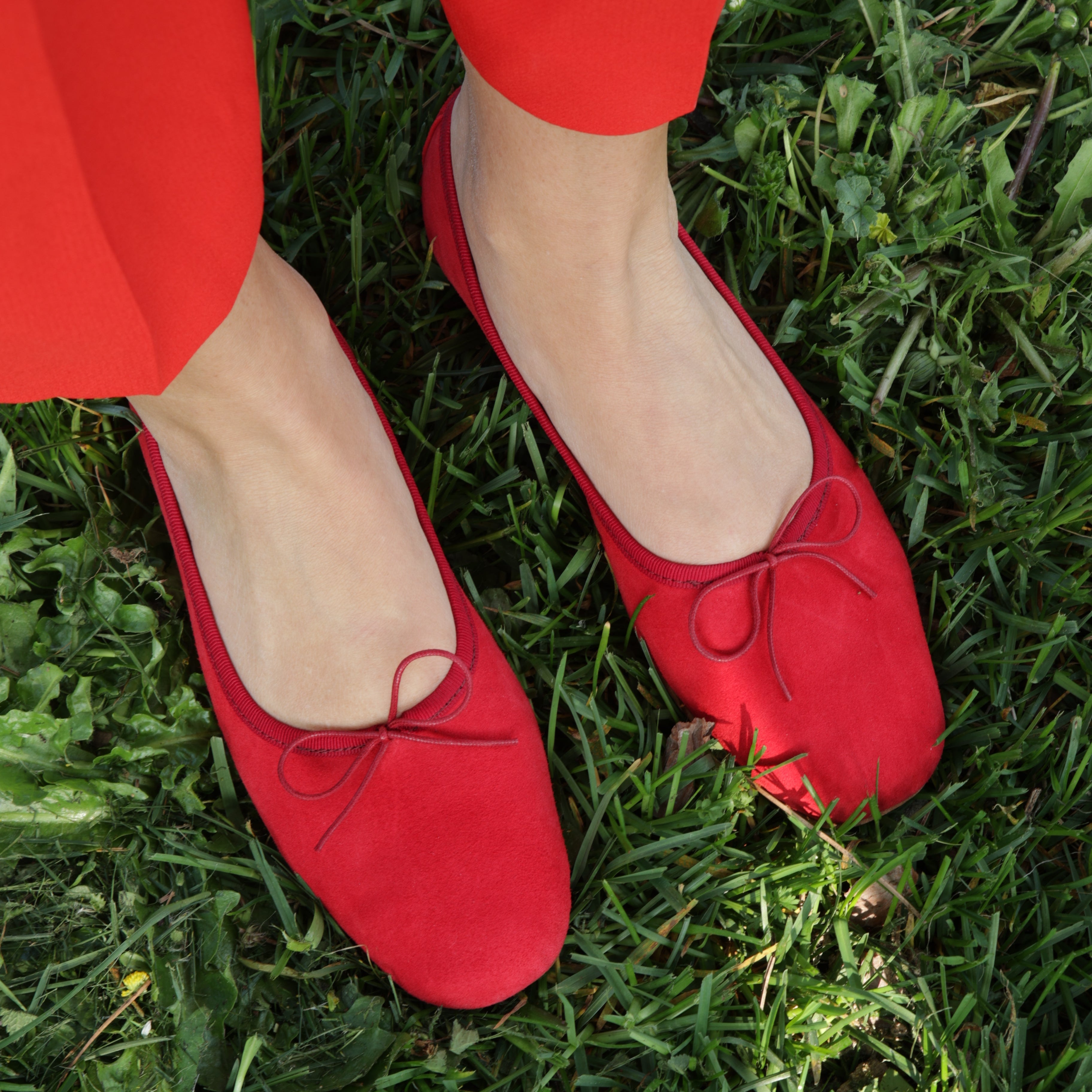Red suede ballerina shoes on a person standing on grass