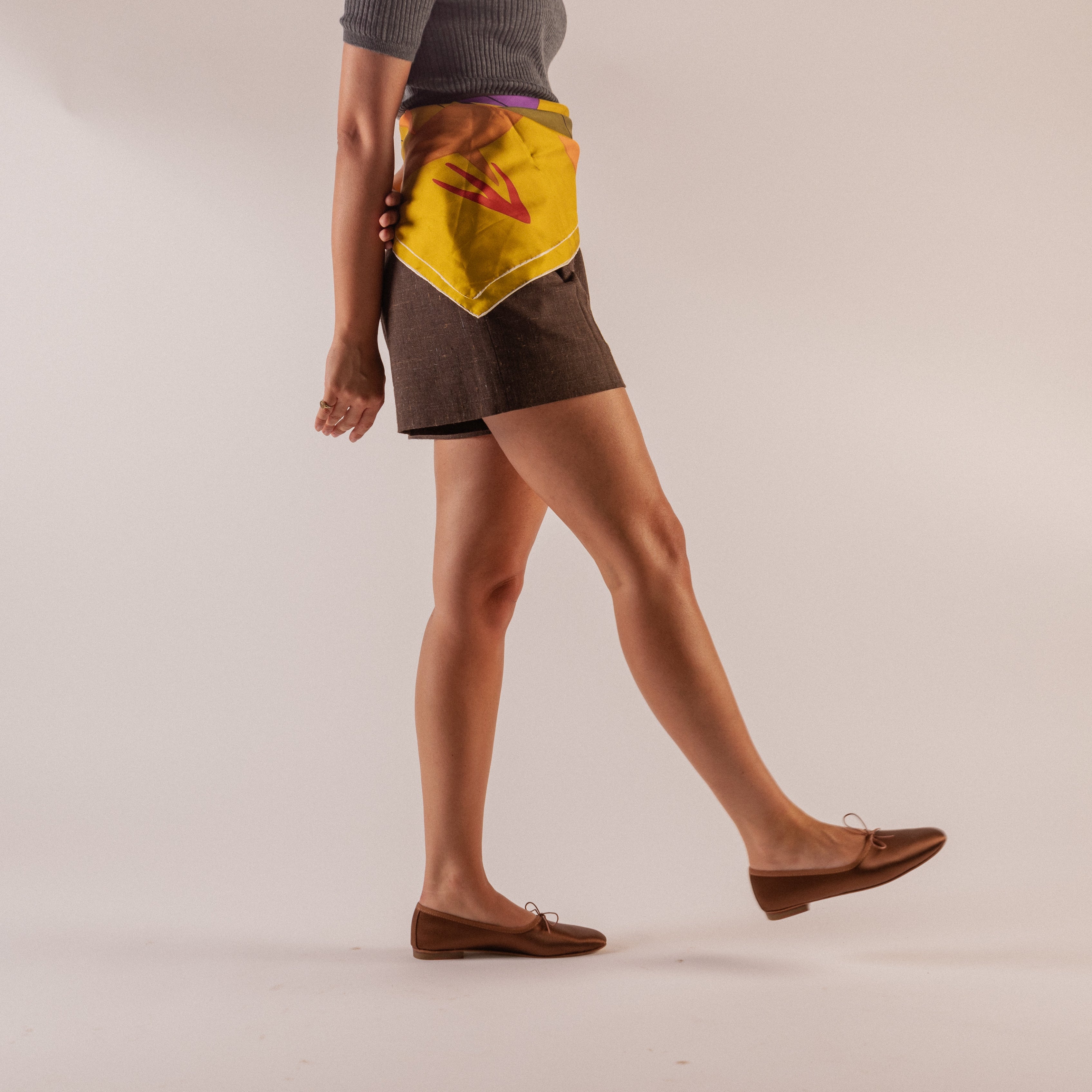 Person wearing satin chocolate ballerina flats on a plain background