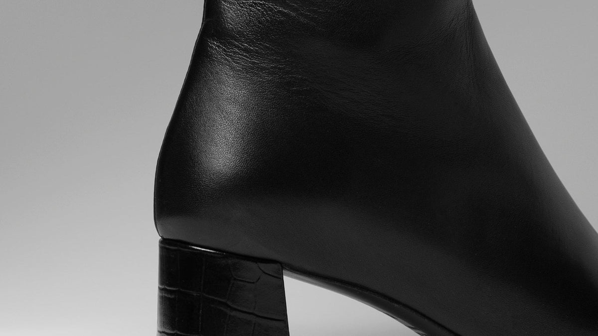 Black leather ankle boot on a gray background