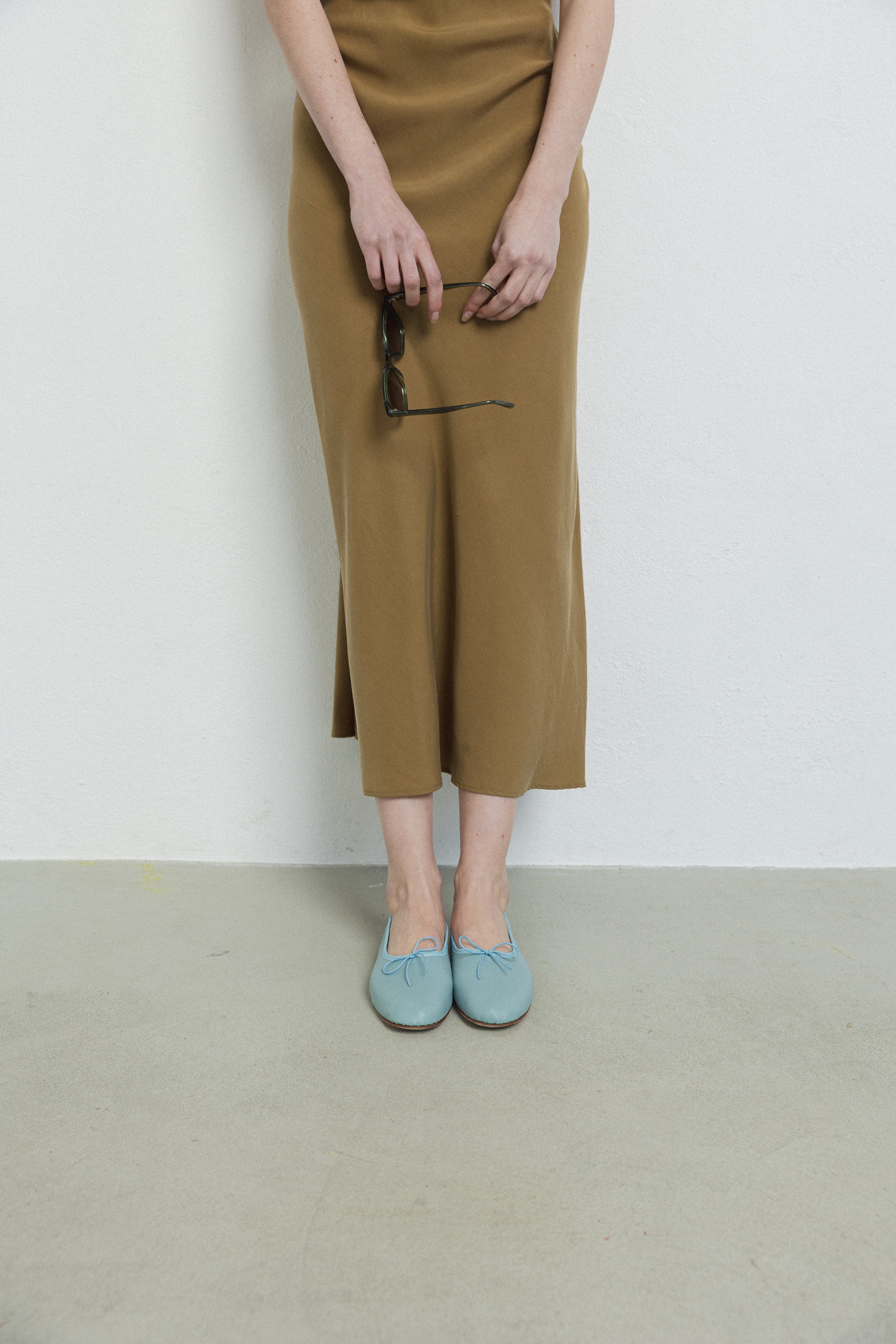 Person wearing a brown skirt and blue shoes on a plain background