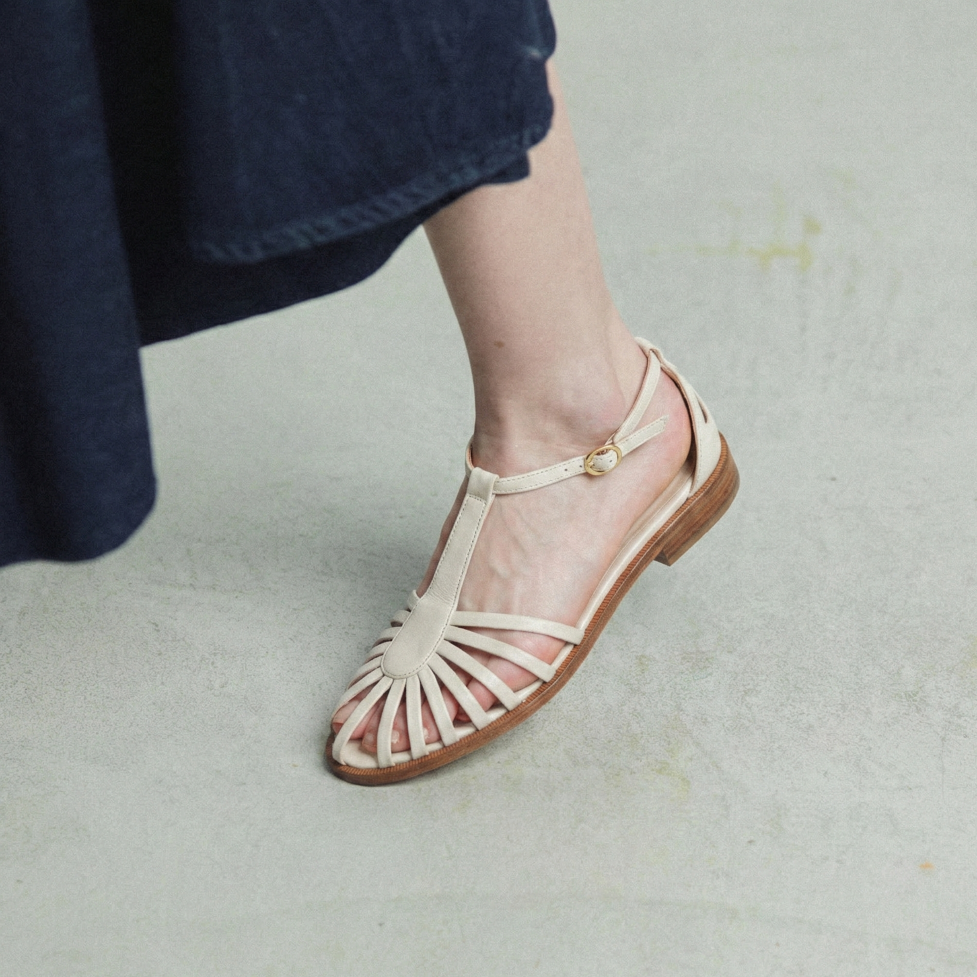Beige sandal with brown sole worn by a person on a light gray background